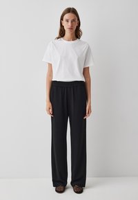 Witte katoenen T-shirt met korte mouwen, gecombineerd met zwarte wijde broek met elastische tailleband en gestructureerde zwarte instappers.