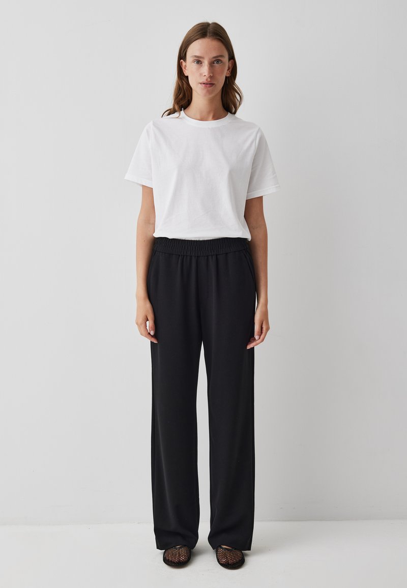 Witte katoenen T-shirt met korte mouwen, gecombineerd met zwarte wijde broek met elastische tailleband en gestructureerde zwarte instappers.