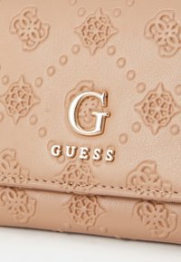 Beige synthetic wallet featuring a textured pattern of floral designs, embossed hardware logo, and a smooth finish with stitching detail.