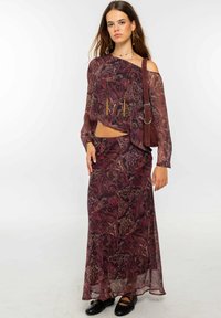 Conjunto fluido y estampado de dos piezas en burdeos y dorado, que incluye una blusa corta de un solo hombro y una falda larga a juego.