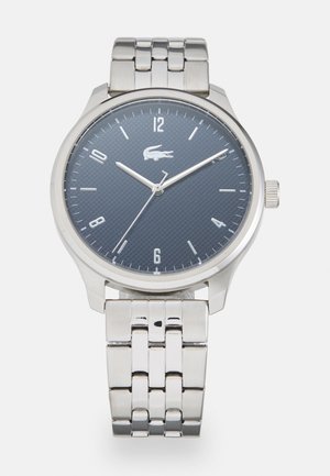 Montre en acier inoxydable argenté avec un cadran rond texturé bleu marine, des index horaires argentés et un bracelet en métal classique à maillons.