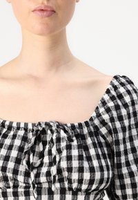 Black and white checked blouse with a square neckline, gathered texture, and tie detail at the center front, made from lightweight fabric.