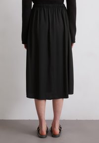 Gonna nera midi con una vita elastica, tessuto fluido e una texture uniforme, abbinata a sandali neri senza lacci.