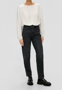 Maglia bianca a maniche lunghe con tessuto strutturato; jeans in denim nero a vita alta; abbinati a scarpe nere lucide. Vestibilità semplice e rilassata.