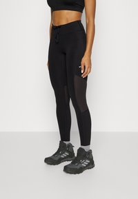 Black athletic leggings with mesh panel accents, high waistband, and drawstring detail. Paired with rugged black sneakers.