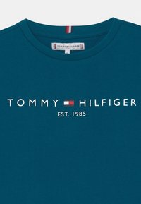 Teal cotton t-paita, jossa on pyöreä kaula-aukko ja voimakas valkoinen teksti logo: "TOMMY HILFIGER EST. 1985" sekä värillinen korostuslogo.