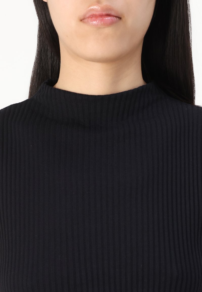 Schwarzes Rippenshirt mit hohem Kragen und strukturiertem Stoff. Das Design ist figurbetont und hebt Einfachheit und Vielseitigkeit hervor.