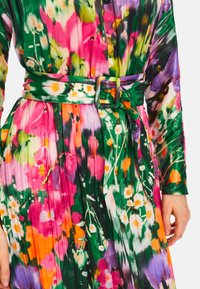 Blumenkleid mit Falten, in lebhaften Farben wie Pink, Grün und Orange. Inklusive einem passenden Gürtel und langen Ärmeln.
