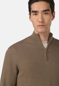 Brązowy sweter z dzianiny z dekoltem na ćwierć zamka, teksturowanym materiałem i ściągaczem przy szyi. Lekka konstrukcja, idealna do warstwowego noszenia.