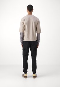 Camiseta de manga corta beige, camiseta de manga larga gris debajo, pantalones cargo negros y zapatos marrones con acentos en blanco y amarillo.