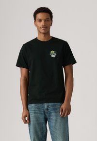 Svart bomull t-skjorte med broderi på fronten av en sol og planter, rund hals, korte ermer og en avslappet passform. Kombinert med blå jeans.