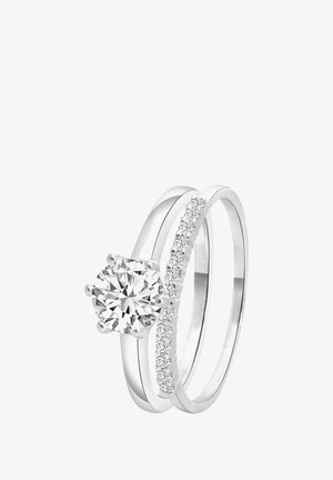 Two interlocking silver rings; one features a large round diamond, the other has a row of small diamonds along its band.