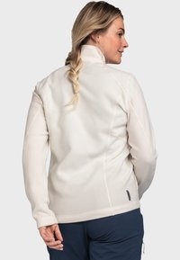 Fleecejacke in Creme mit hohem Kragen, tailliertem Design und kontrastierenden Nähten. Verfügt über einen leichten Stretch und ein Etikett an der Seite.
