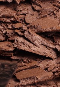 Wiórki czekoladowe o różnych rozmiarach i kształtach, prezentujące bogaty brązowy kolor oraz lekko teksturowaną powierzchnię.