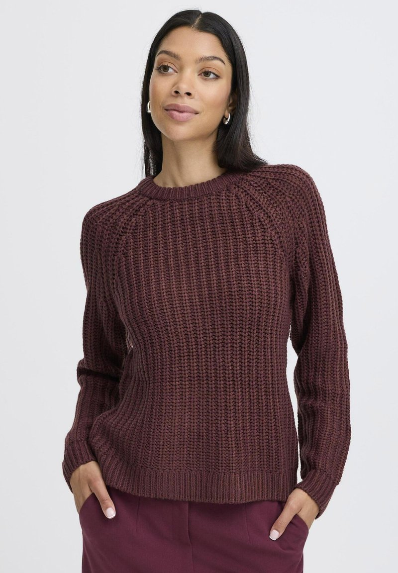 Bordeauxfarbener Strickpullover mit geripptem Muster, Rundhalsausschnitt, langen Ärmeln und lässiger Passform, kombiniert mit lila Hosen.
