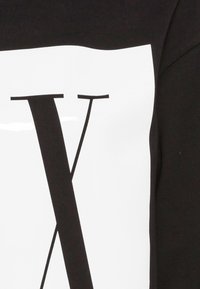 Svart sweatshirt med en stor vit grafik och ett framträdande svart bokstav "V". Tillverkad av ett mjukt, texturerat tyg.