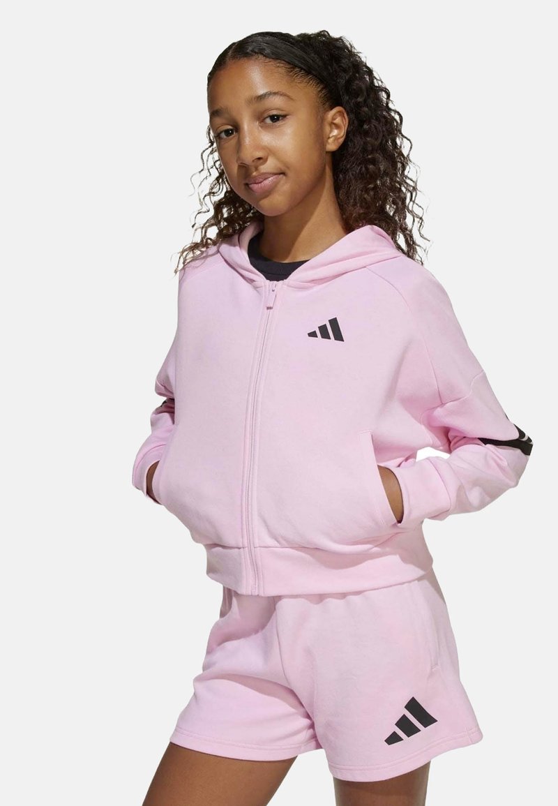 Sudadera con cremallera de color rosa claro con acentos y logotipo negros, combinada con pantalones cortos rosa a juego. Tejido suave, corte casual y diseño con capucha.