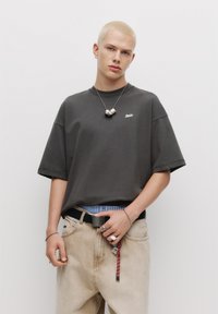 Mørkegrå oversized t-shirt med korte ærmer, rund hals og lille logo. Bæret med lysebeige jeans og et sort bælte, samt tilbehør.