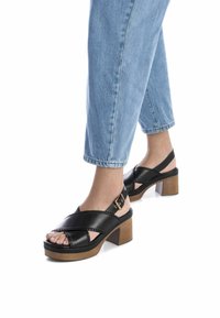 Zwarte leren platform sandalen met een gekruisd bandjesontwerp en een houten blokhak. Versierd met een metalen gesp aan de zijkant.