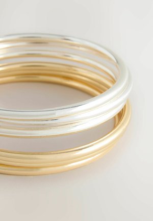 Set aus drei glatten metallischen Armreifen, die abwechselnd in Silber- und Goldtönen gehalten sind. Kreisförmige Form mit einer polierten Oberfläche und reflektierendem Finish.