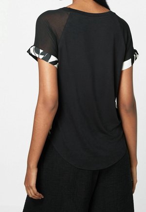 T-shirt nera con orlo arrotondato e schiena trasparente. Le maniche corte presentano un motivo a foglie in contrasto bianco e nero sui polsini.