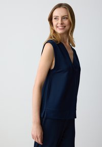 Top senza maniche blu navy con scollatura a V. Tessuto liscio, vestibilità rilassata e un sottile dettaglio cucito all'orlo.