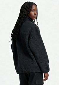 Maglione in pile nero con superficie strutturata e pannello liscio nero sulle spalle. Vestibilità ampia e maniche lunghe.