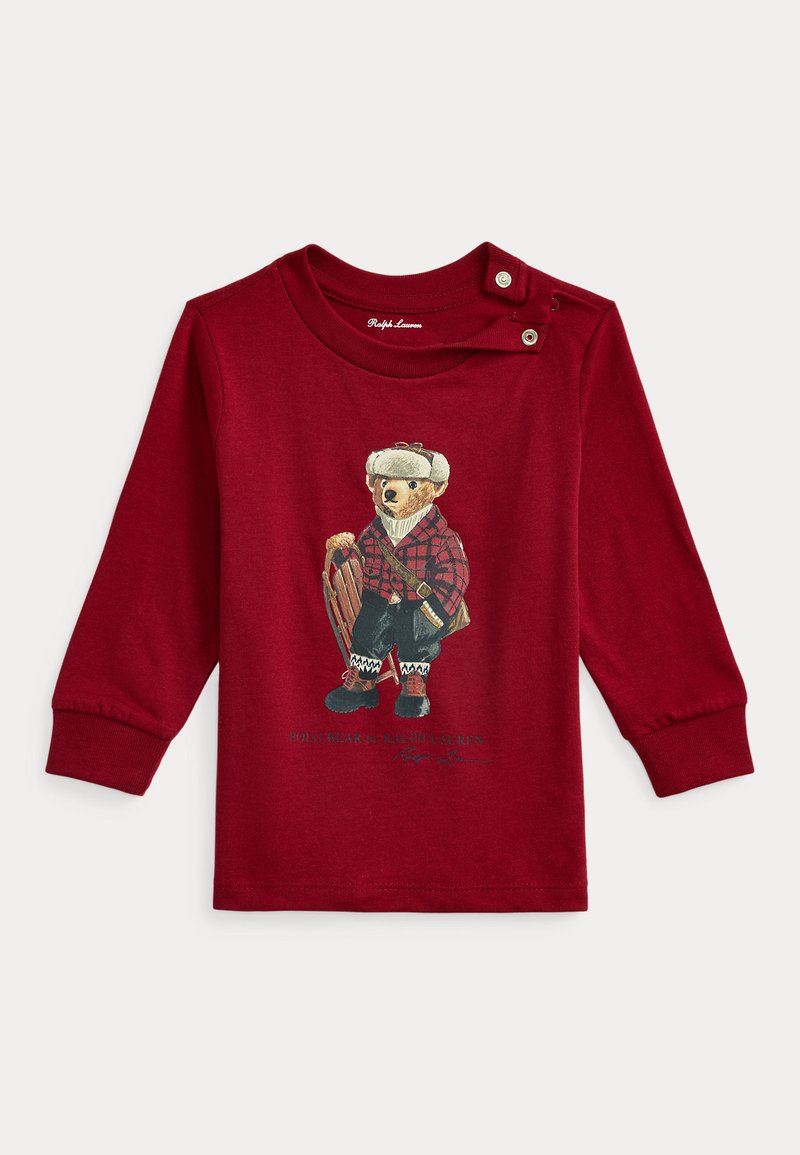 Piros hosszú ujjú póló, téli ruhás medve grafikával, kockás részletekkel és szánkóval, valamint patenttal az vállnál.