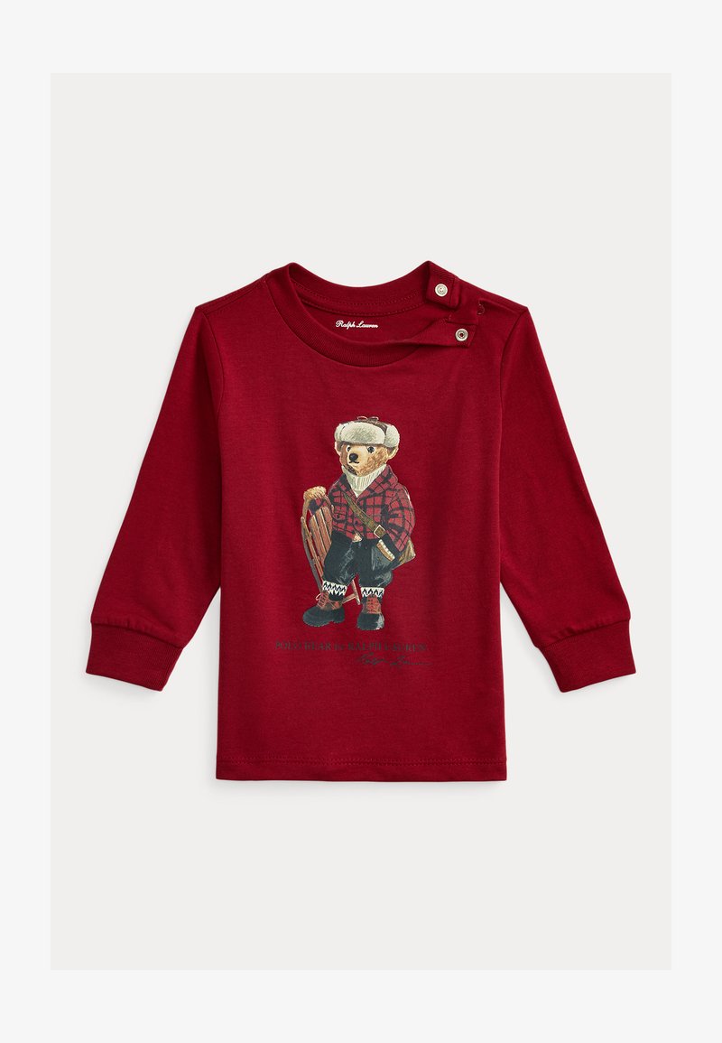 Piros hosszú ujjú póló, téli ruhás medve grafikával, kockás részletekkel és szánkóval, valamint patenttal az vállnál.