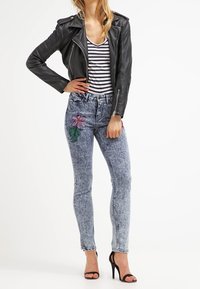 Czarna skórzana kurtka motocyklowa założona na bluzkę w paski, do tego jasnoniebieskie dżinsy z kwiatowymi haftami. Całość dopełniają cienkie sandały na obcasie.