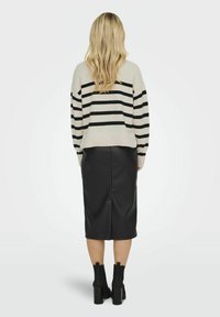 Gestreifter, schwarz-weißer Strickpullover im Crop-Design, kombiniert mit einem schwarzen Bleistiftrock aus Kunstleder und schwarzen, hochhackigen Stiefeletten.