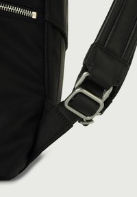 Borsa a tracolla nera in nylon e pelle con una fibbia metallica argentata. La tracolla presenta una finitura testurizzata e dettagli di cucitura visibili.