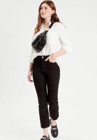 Jean taille haute noirs avec une légère évasement, associés à une chemise blanche à boutons. Un sac en cuir noir porté en travers met en valeur le look.