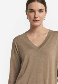 Beige V-ringad tröja gjord av mjukt material, med en avslappnad passform och ribbade kanter, som har en slät textur och minimal detaljering.