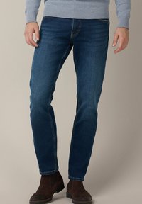 Granatowe dżinsy o slim fit, z jasnym przeszyciem, bocznymi kieszeniami i subtelnym wyblyskaniem. Połączone z brązowymi botkami za kostkę.