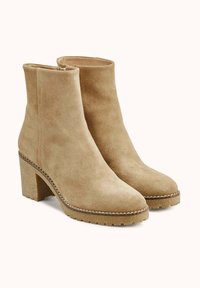 Bottines en daim beige avec un talon bloc, un bout rond et des détails cousus le long de la semelle ; surface texturée et design minimaliste.
