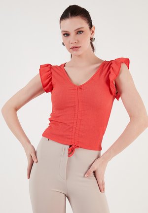 Red smocked top with short ruffled sleeves, V-neckline, and gathered front detail. Paired with beige form-fitting pants. Smooth texture.