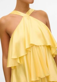 Gul satin kjole med lagdelte flæser og krydsrygdesign. Stoffet ser glat ud med en let glans og delikate kanter.