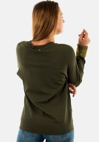 Maglione verde oliva con colletto e polsini a coste, caratterizzato da dettagli metallici sulle maniche e una vestibilità comoda.