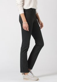 Jeans de mezclilla negra con un corte ajustado y un ligero acampanado en el dobladillo. Llevados con zapatillas grises que tienen un upper texturizado y acentos blancos.