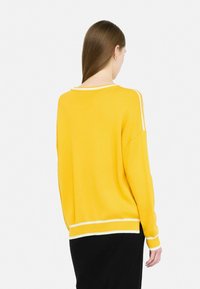 Maglione giallo con strisce bianche sulle spalle e sull'orlo. Texture a maglia morbida. Vestibilità ampia con spalle scese e colletto a coste.
