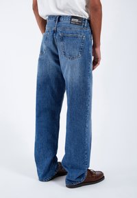 Loose-fit, blue denim jeans with a faded wash. Features back pockets and a black label at the waistband. Slightly distressed texture.