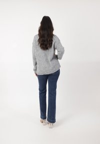 Szary, puszysty sweter z zaokrąglonym dołem, zestawiony z ciemnoniebieskimi jeansami o prostym kroju i sandałami na przeźroczystym obcasie.