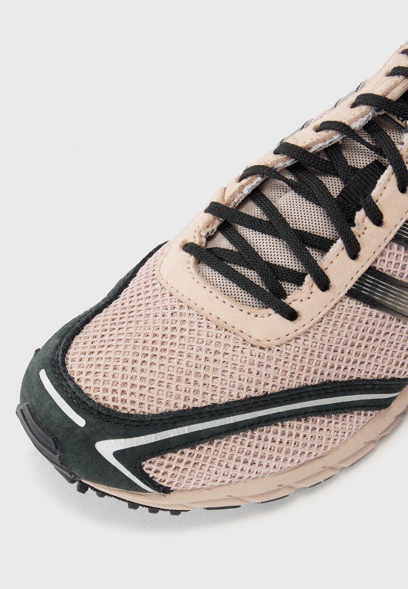 Light pink athletic shoe with mesh upper, black accents, textured surface, and striped detailing. Features black laces and rubber sole.