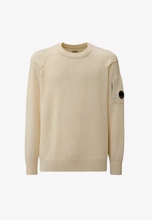 Pull en tricot couleur crème avec un col rond, des bords côtelés au bas et aux poignets, doté d'une poche à rabat sur la manche gauche ornée d'un accent de bouton noir.