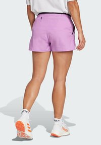 Shorts deportivos color lila con cintura elástica, bolsillos laterales y una textura suave y lisa. Combinados con zapatos blancos con detalles en naranja.