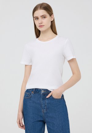 T-shirt bianco in cotone con maniche corte, scollatura rotonda e vestibilità morbida. Abbinato a jeans di denim blu a vita alta.