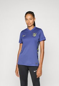 Maglia Nike viola con maniche corte; presenta dettagli gialli e un logo dell'Atlético Madrid. Indossata con pantaloni sportivi neri.