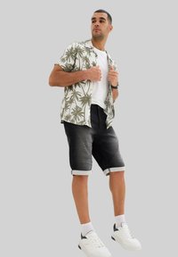 Chemise à manches courtes avec un motif de palmiers en vert et crème, accompagnée de shorts en denim noirs et de baskets blanches avec des accents bleu marine.