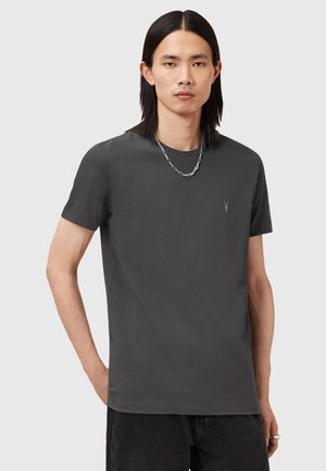 Graues kurzärmliges T-Shirt aus weichem Stoff, mit kleinem Logo auf der Brust und lockerer Passform, kombiniert mit dunklen Jeans.